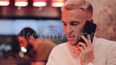年轻的帅哥在夜间咖啡馆的智能手机上聊天。 他坐在霓虹灯招牌旁边喝着鸡尾酒